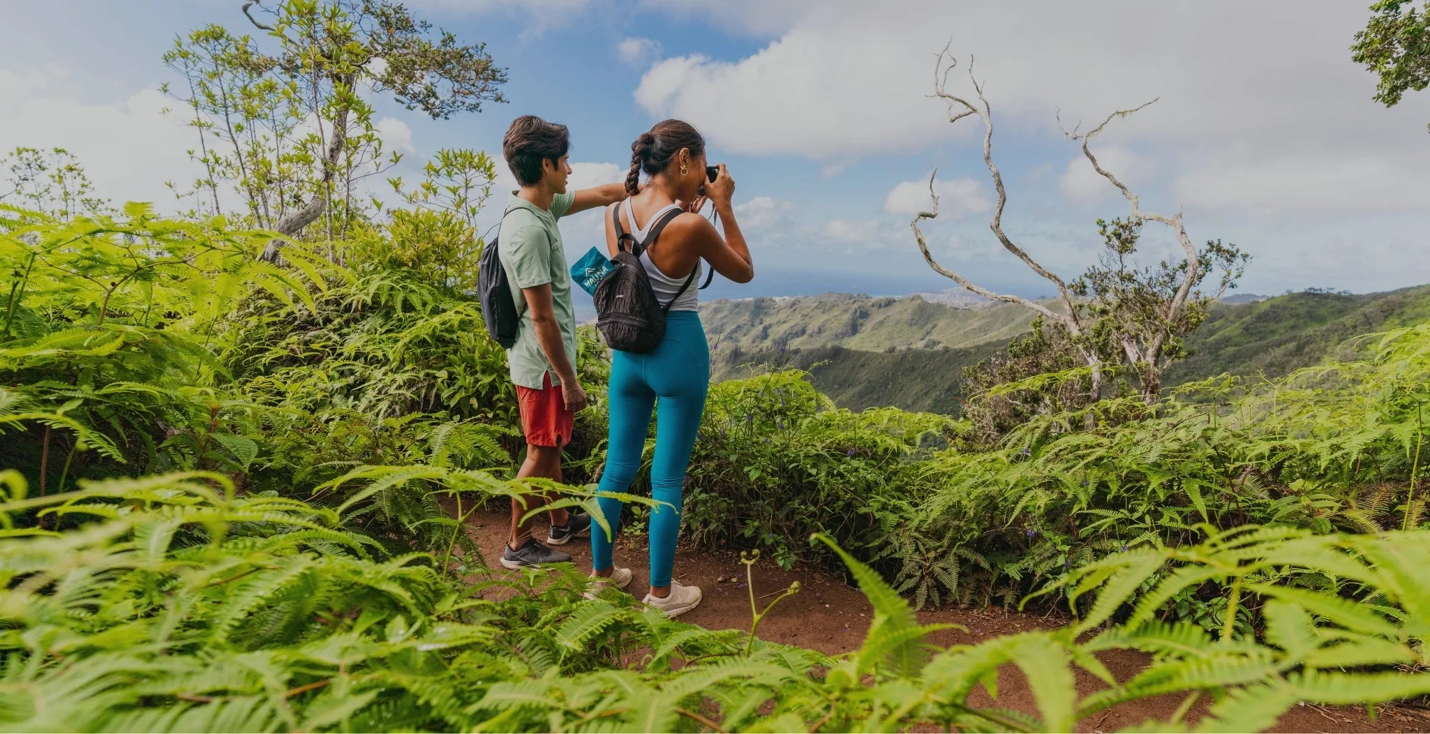 Young man and woman on a mountain trail in hawaii taking pictures of the view.