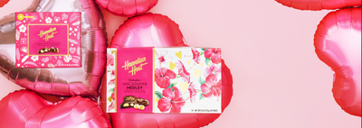 This is an image banner with two boxes of Hawaiian Host products, Island Macs (Valentine's) and Valentine's Macadamia Medley, with pink heart shaped balloons for Valentine's Day.